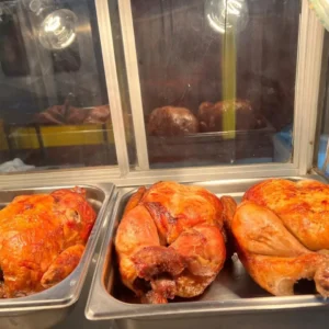 Pollo asado dorado exhibido en bandejas calientes