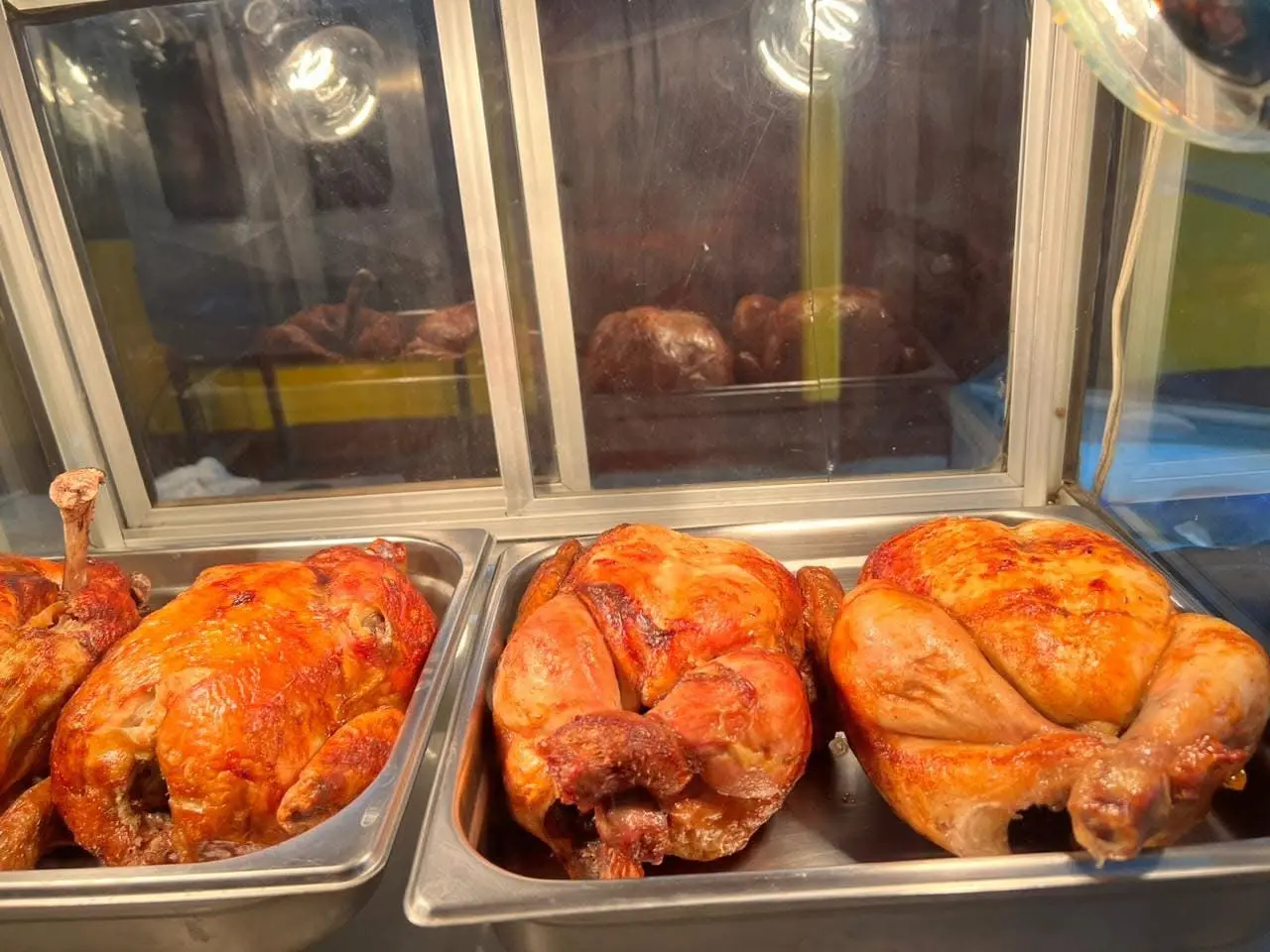 Pollo asado dorado exhibido en bandejas calientes