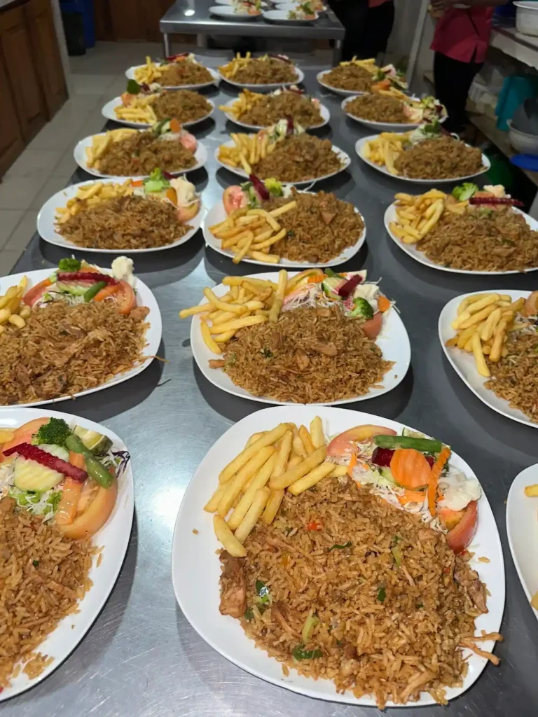 Platos de arroz con pollo preparados para un evento y servidos con ensalada y papas fritas.
